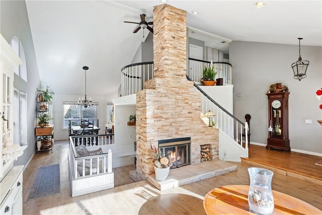 living room with ceiling fan with notable chandelier, hardwood / wood-style floors, high vaulted ceiling, and a fireplace