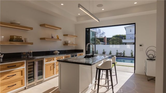 kitchen featuring a breakfast bar, sink, an island with sink, light brown cabinetry, and beverage cooler