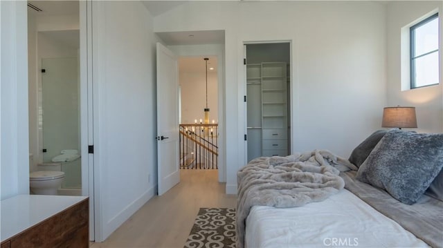 bedroom with a notable chandelier, light hardwood / wood-style flooring, a spacious closet, connected bathroom, and a closet