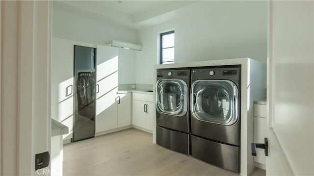 clothes washing area with light hardwood / wood-style flooring, washing machine and dryer, and cabinets