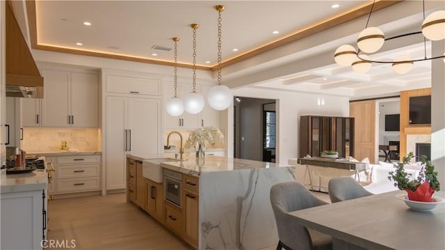 kitchen featuring a spacious island, white cabinets, hanging light fixtures, light stone counters, and sink