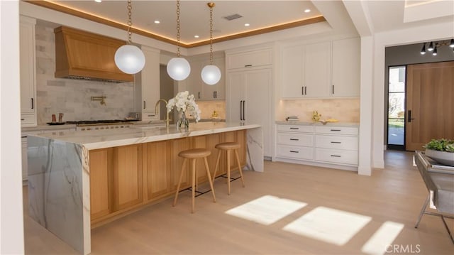 kitchen featuring white cabinetry, pendant lighting, backsplash, and a tray ceiling