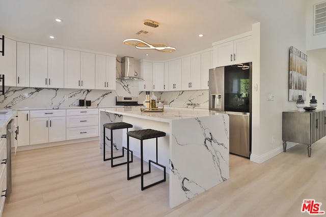 kitchen featuring stainless steel refrigerator with ice dispenser, a center island, light stone countertops, white cabinets, and wall chimney range hood