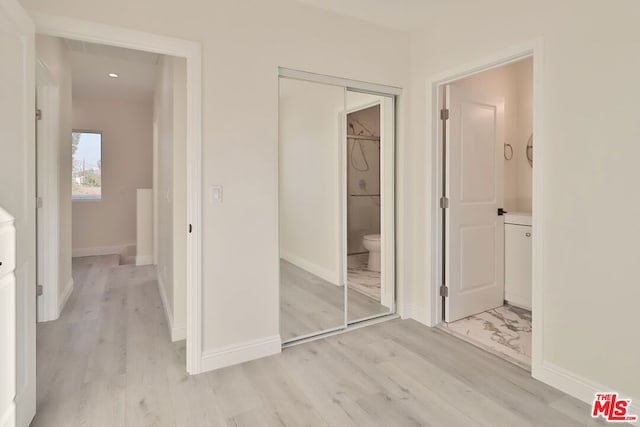 unfurnished bedroom featuring a closet, light hardwood / wood-style floors, and connected bathroom