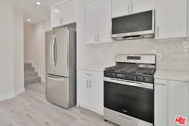 kitchen with white cabinets, light wood-type flooring, backsplash, and stainless steel appliances