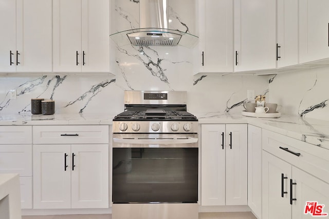 kitchen with light stone counters, white cabinetry, island range hood, and gas stove