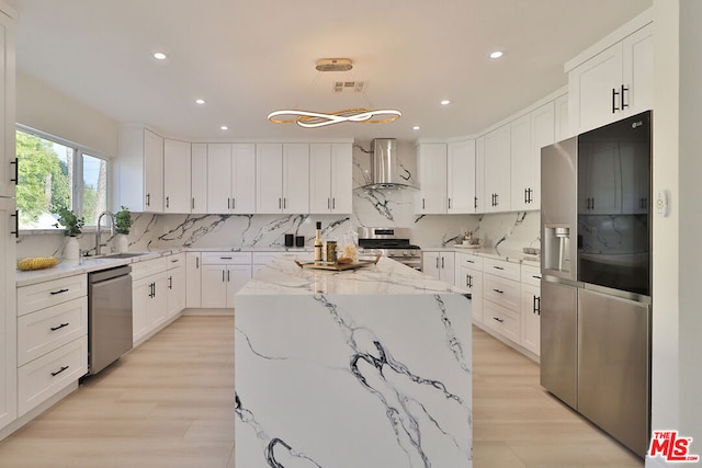 kitchen with a center island, stainless steel appliances, white cabinets, wall chimney exhaust hood, and light stone counters