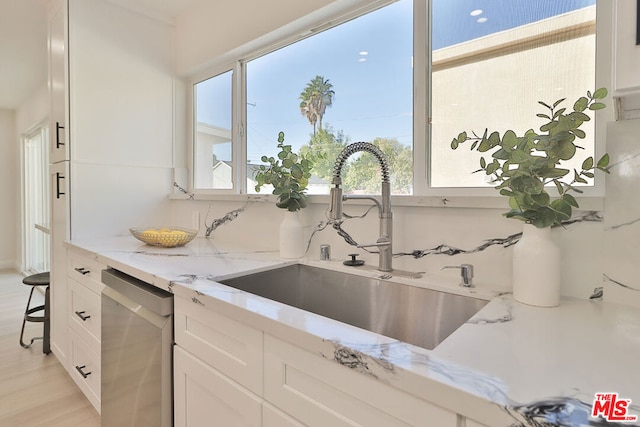 kitchen featuring white cabinetry, light hardwood / wood-style floors, light stone countertops, stainless steel dishwasher, and sink