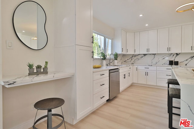 kitchen with a kitchen breakfast bar, light stone countertops, stainless steel dishwasher, white cabinets, and sink