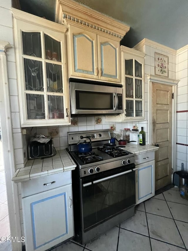 kitchen with light tile patterned floors, backsplash, appliances with stainless steel finishes, and tile counters