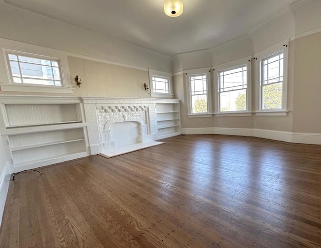 unfurnished living room featuring dark wood-type flooring, built in shelves, and a brick fireplace