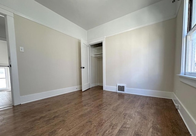 unfurnished bedroom featuring multiple windows, dark hardwood / wood-style flooring, and a closet