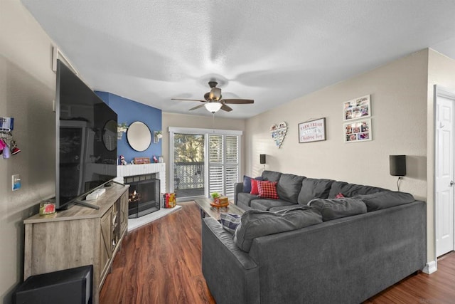 living room featuring ceiling fan, a textured ceiling, dark hardwood / wood-style flooring, and a brick fireplace