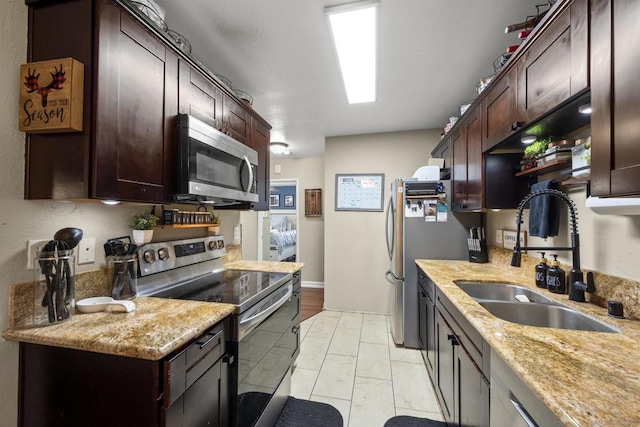 kitchen with sink, light tile patterned flooring, dark brown cabinetry, light stone countertops, and stainless steel appliances