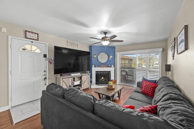 living room with a textured ceiling, ceiling fan, a fireplace, and wood-type flooring