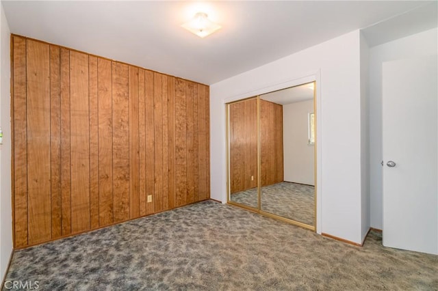 unfurnished bedroom with carpet floors, a closet, and wooden walls