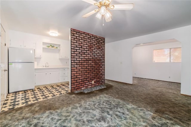 unfurnished living room featuring ceiling fan, sink, and dark colored carpet