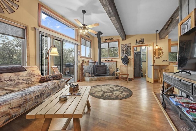 living room featuring beamed ceiling, ceiling fan, light hardwood / wood-style flooring, and a wood stove