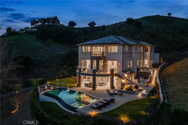 back house at dusk with a patio area, a balcony, and a yard