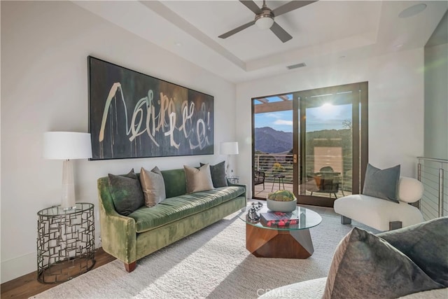 living room with a raised ceiling, ceiling fan, a mountain view, and hardwood / wood-style floors