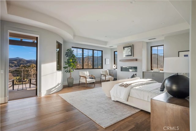 bedroom featuring hardwood / wood-style floors, a raised ceiling, access to outside, a mountain view, and multiple windows