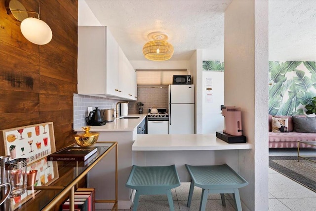 kitchen with kitchen peninsula, decorative backsplash, sink, white appliances, and white cabinetry