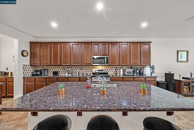 kitchen featuring dark stone countertops, a breakfast bar, appliances with stainless steel finishes, and an island with sink