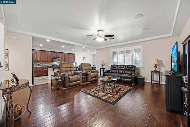 living room featuring dark wood-type flooring, ceiling fan, and a raised ceiling