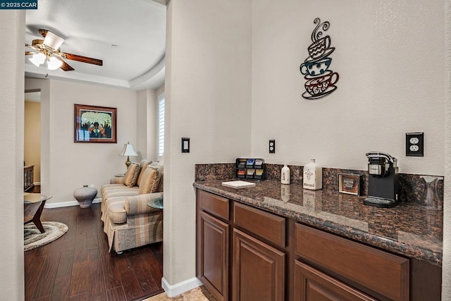 bar featuring ceiling fan, dark stone countertops, a raised ceiling, and hardwood / wood-style flooring