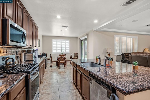 kitchen featuring dark stone countertops, a center island with sink, a wealth of natural light, sink, and stainless steel appliances