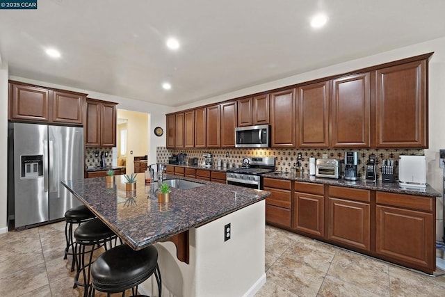 kitchen with an island with sink, appliances with stainless steel finishes, dark stone counters, a breakfast bar, and sink