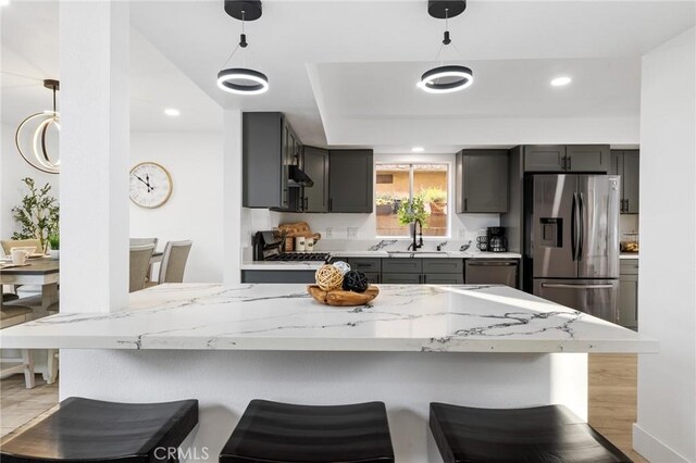 kitchen with light stone countertops, decorative light fixtures, stainless steel appliances, sink, and a breakfast bar