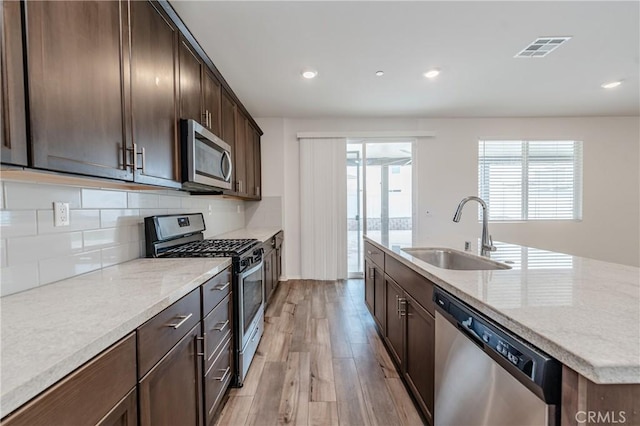 kitchen featuring sink, light hardwood / wood-style flooring, stainless steel appliances, light stone counters, and tasteful backsplash