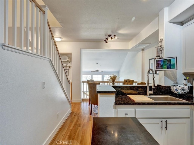 kitchen featuring ceiling fan, light hardwood / wood-style floors, sink, white cabinetry, and dark stone counters