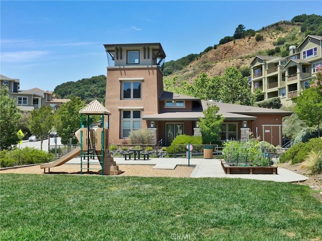 rear view of property featuring a playground, a mountain view, and a lawn