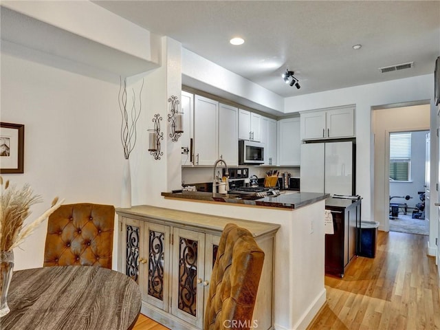 kitchen with light hardwood / wood-style floors, kitchen peninsula, a breakfast bar area, stove, and white refrigerator