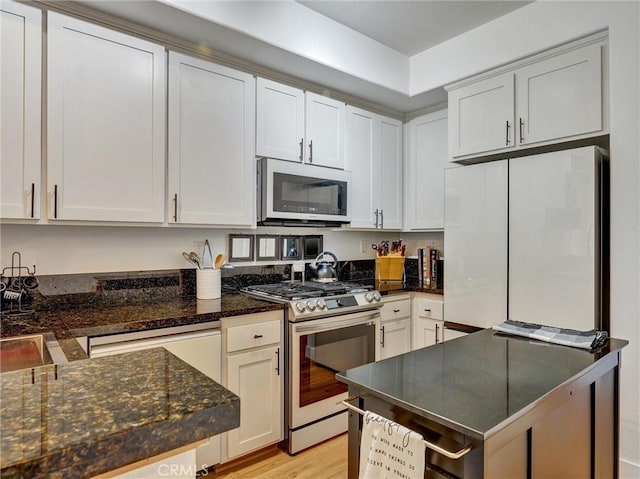 kitchen with stainless steel range with gas cooktop, white cabinetry, white fridge, and dark stone countertops