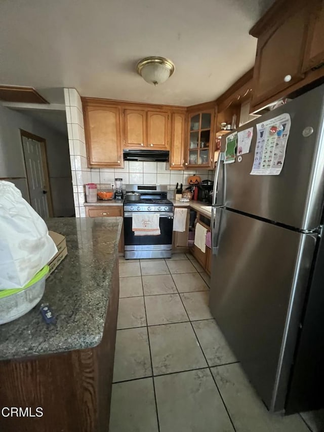 kitchen featuring stainless steel appliances, dark stone counters, light tile patterned flooring, and backsplash