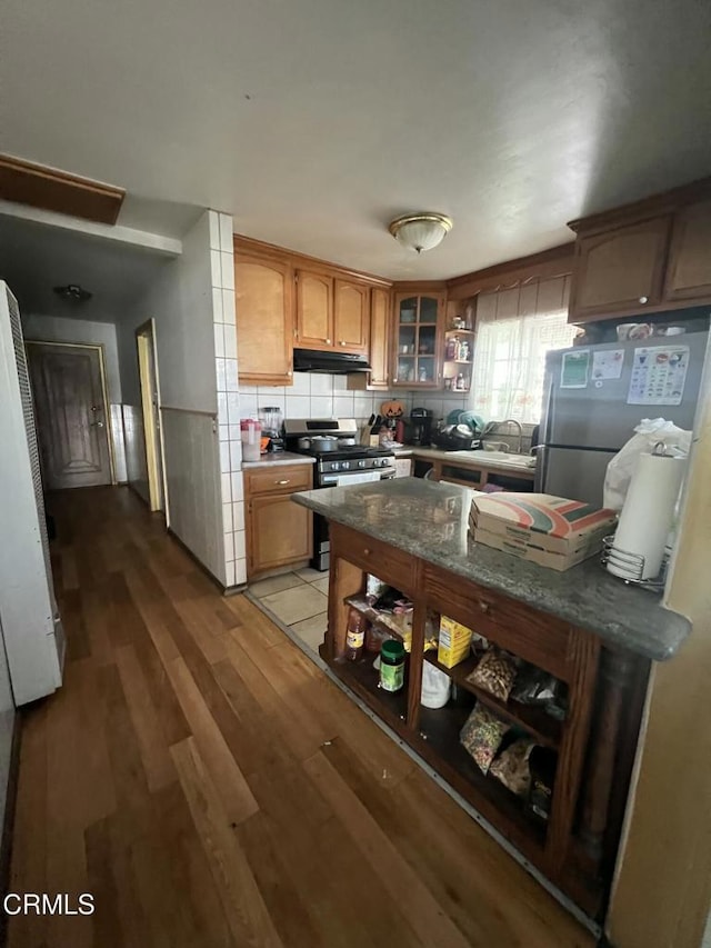 kitchen featuring sink, light wood-type flooring, decorative backsplash, dark stone counters, and appliances with stainless steel finishes