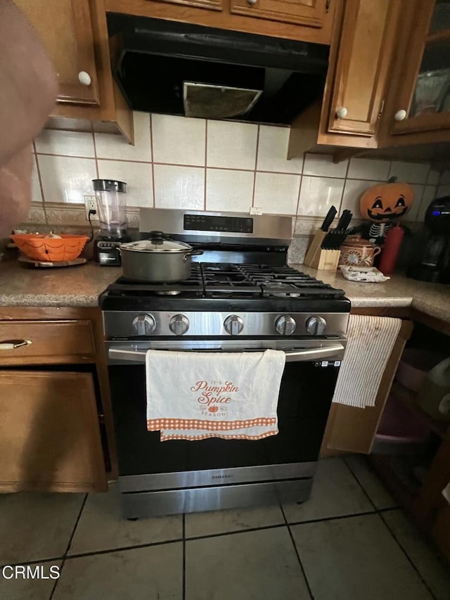 kitchen featuring gas range, tile patterned flooring, extractor fan, and decorative backsplash