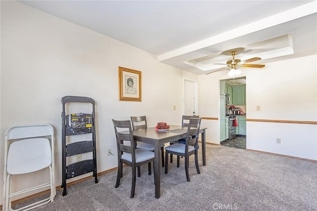 carpeted dining area with ceiling fan and a raised ceiling