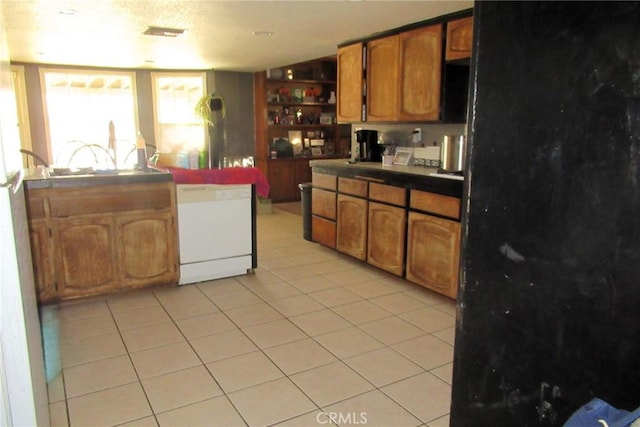 kitchen featuring visible vents, brown cabinetry, dark countertops, white dishwasher, and light tile patterned flooring