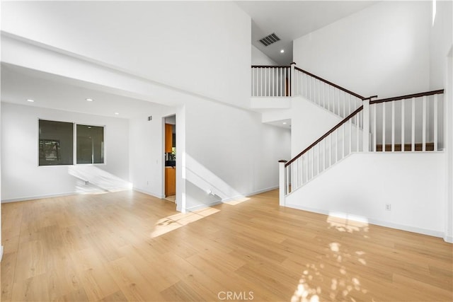 unfurnished living room featuring light hardwood / wood-style floors and a towering ceiling