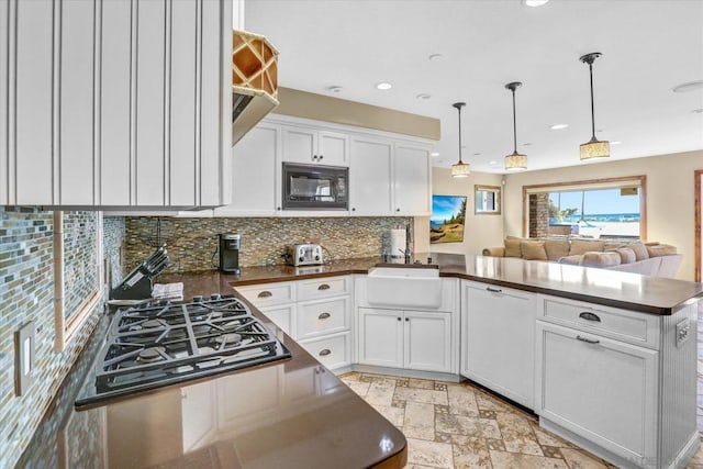 kitchen featuring black microwave, backsplash, white cabinets, and hanging light fixtures