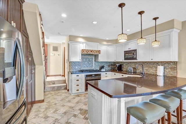 kitchen featuring stainless steel appliances, kitchen peninsula, a breakfast bar area, and decorative light fixtures