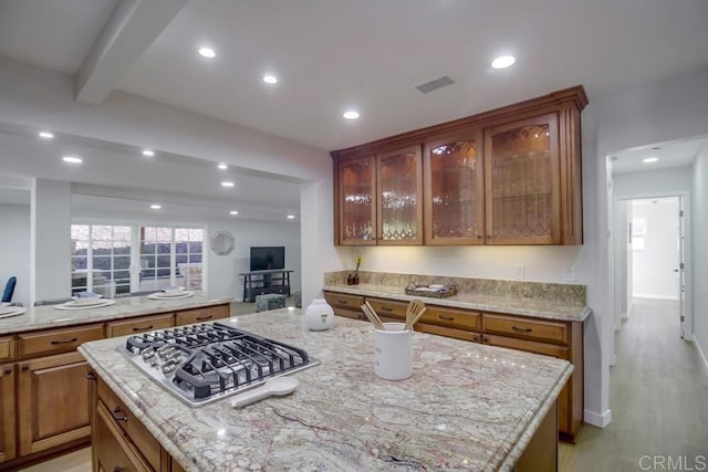 kitchen featuring a center island, light hardwood / wood-style flooring, light stone counters, stainless steel gas stovetop, and beam ceiling