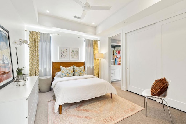 bedroom featuring light carpet, ceiling fan, a tray ceiling, and ensuite bath