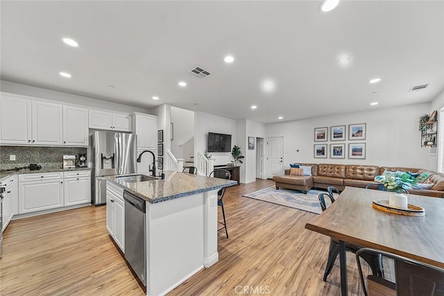 kitchen with light hardwood / wood-style floors, an island with sink, appliances with stainless steel finishes, stone countertops, and white cabinets