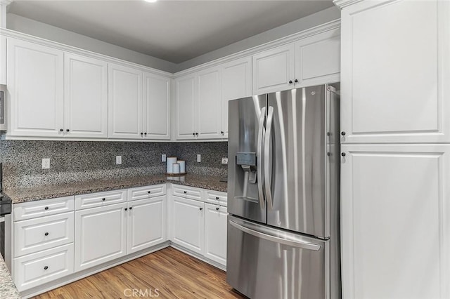 kitchen with white cabinetry, light hardwood / wood-style floors, appliances with stainless steel finishes, backsplash, and dark stone countertops