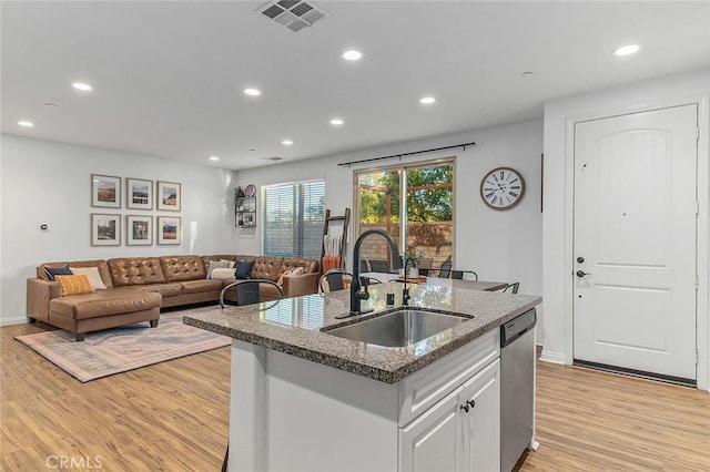 kitchen with white cabinets, dishwasher, sink, light wood-type flooring, and a center island with sink